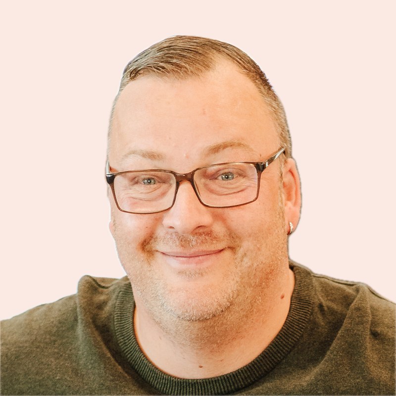 Marcel Lübke lächelt in die Kamera. Er trägt eine Brille und einen olivgrünen Pullover.
